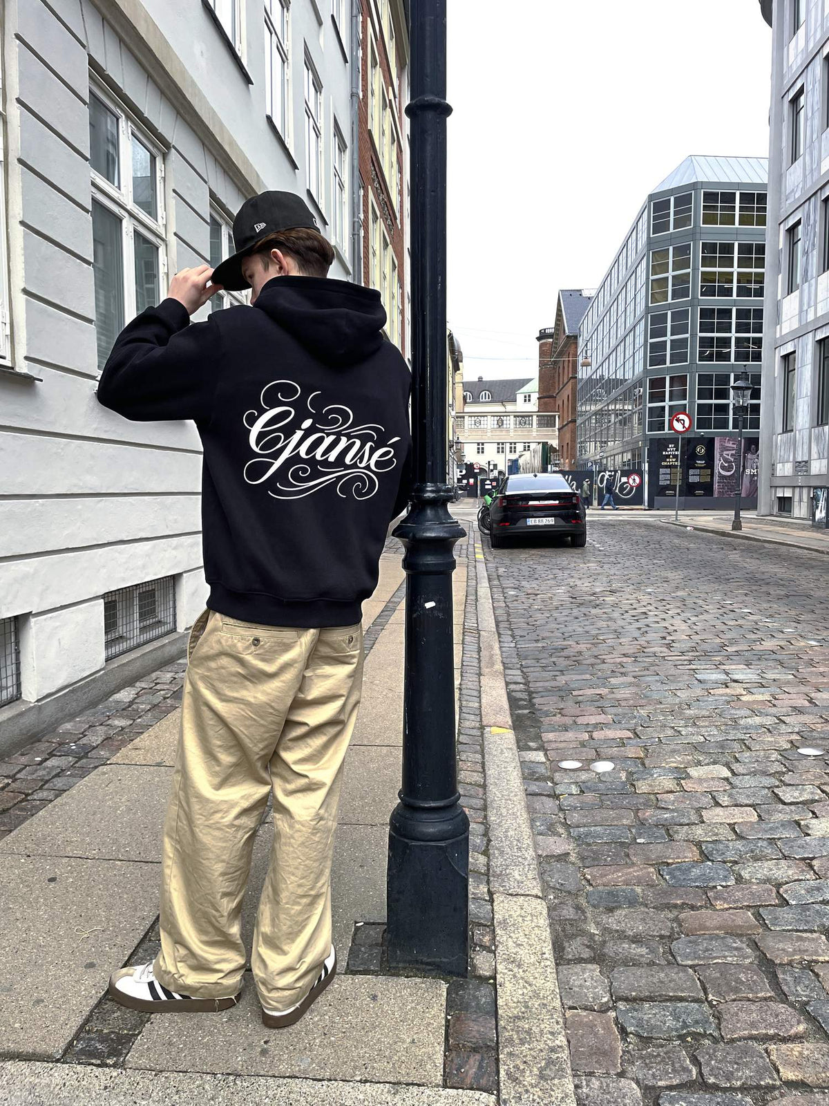 ORIGIN 001 set bagfra på model: sort hoodie med hætte og stort script-print på ryggen