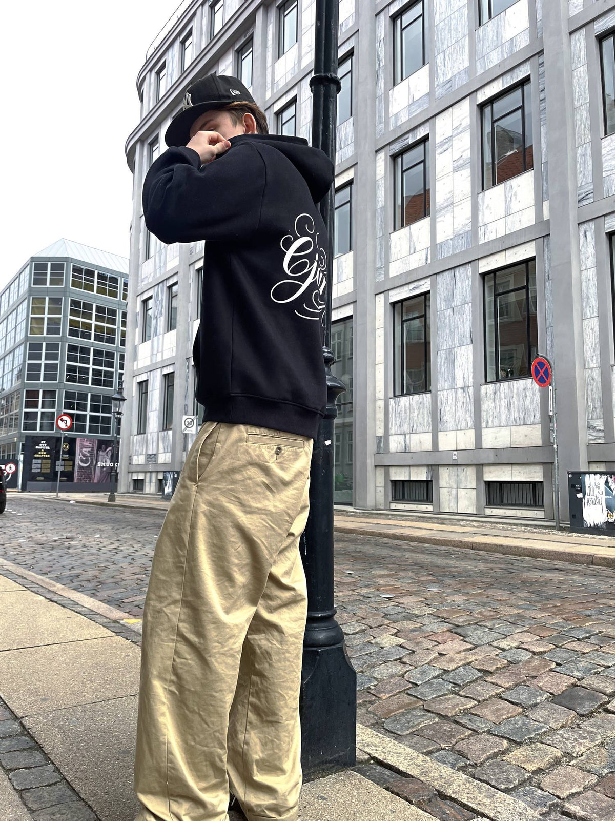 Sort Ejansé hoodie set fra siden, der viser den boxy pasform, ribkanten i taljen og rygprintet